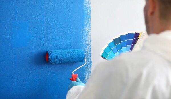 Craftsman holds roller and a color palette and paints white wall blue